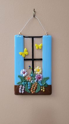 a blue window with flowers and butterflies hanging on the wall next to a planter