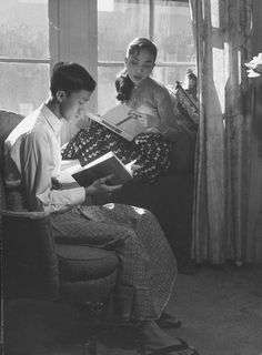 an old photo of two people sitting on a couch and one is reading a book