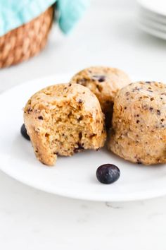 three blueberry muffins on a white plate with fresh blueberries around them