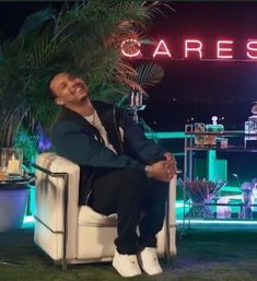 a man sitting on top of a white chair in front of a neon sign