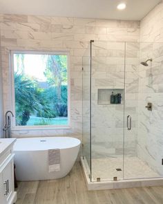 a white bath tub sitting next to a window in a bathroom with marble walls and floors