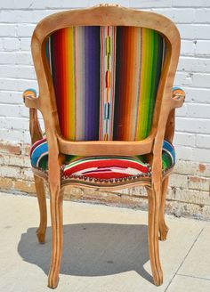 an old wooden chair with colorful striped fabric on it's armrests and back