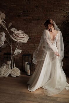 a woman in a wedding dress standing next to a brick wall with flowers on it