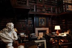 a room filled with lots of books next to a bust of a man in front of a fireplace