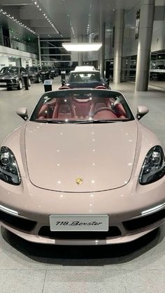 a pink sports car is parked in a showroom filled with other cars and people