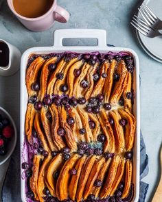 a casserole dish filled with blueberries and peaches, next to two cups of coffee