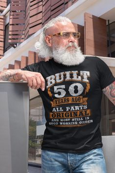 an older man with white hair and beard wearing a t - shirt that says built 50 years ago