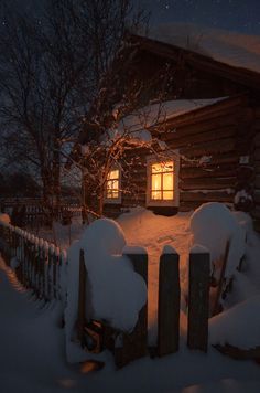 a log cabin with snow on the ground and windows lit up in the night sky