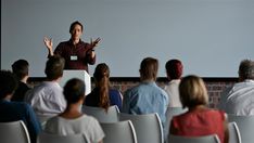 a woman standing in front of a crowd while giving a presentation to the people behind her