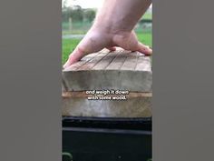 a person's hand reaching over the edge of a piece of wood on top of a picnic table