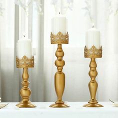 three gold candles are sitting next to each other on a table with white linens