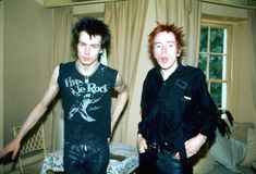 two young men standing next to each other in front of a living room with curtains