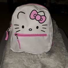 a white hello kitty backpack sitting on top of a furry surface with a pink bow