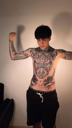 a man with tattoos on his body standing in front of a wall and posing for the camera