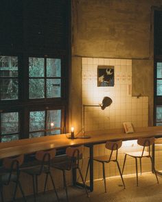 a long table with two chairs next to it in front of some windows and candles