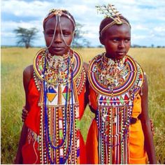 two young women in traditional african dress standing next to each other on the grass field