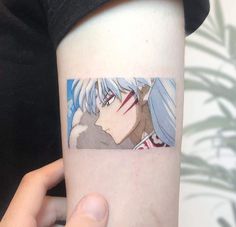 a person with a tattoo on their arm holding up a piece of paper that has an anime character drawn on it