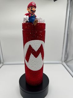 a red and white cup with a mario figure on it's top in a display case