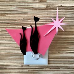 a pink light switch cover with two black cats on it's side and a star hanging from the wall