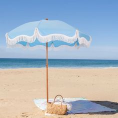 an umbrella on the beach with a bag under it and blue water in the background