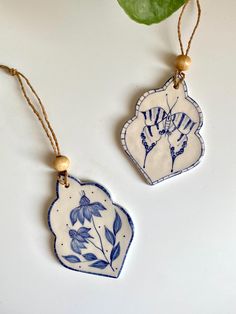 two blue and white ceramic ornaments hanging from strings on a table next to a green leaf