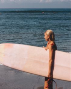 a man holding a pink surfboard on top of a beach next to the ocean