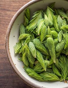 a bowl filled with green leaves on top of a wooden table