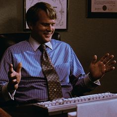 a man sitting in front of a computer desk with his hands out to the side