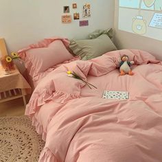 a bed with pink sheets and pillows in a room next to a wall with pictures on it