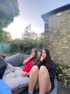 two women sitting on a couch in the backyard