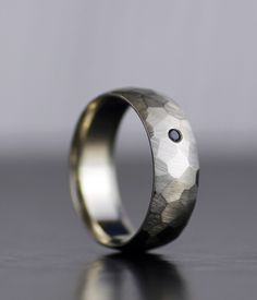 a wedding ring with a black diamond in the center on a gray surface, sitting on top of a table