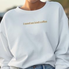 a woman wearing a white sweatshirt with the words i need an iced coffee printed on it