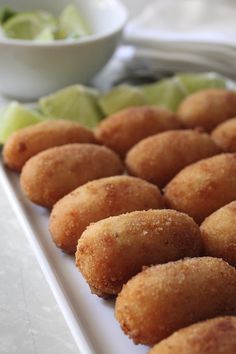 some fried food on a white plate with limes and a bowl in the background