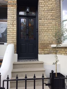 a black front door on a brick house with white stairs and planter next to it