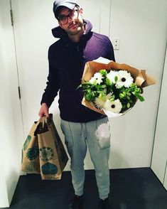 a man is holding flowers and bags in an elevator area while looking at the camera