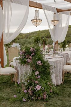 an outdoor dining area with tables and chairs covered in white drapes, flowers and greenery