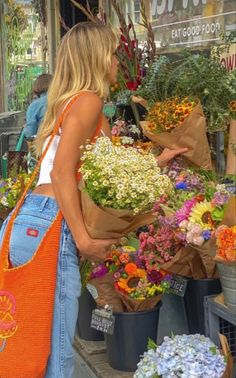 a woman standing in front of a bunch of flowers with a bag on her shoulder