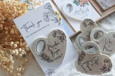 four heart - shaped buttons with thank you written on them next to a card and some dried flowers