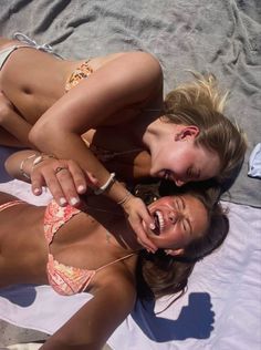 two women in bikinis are laying on the beach and one has her mouth open