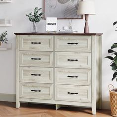 a white dresser sitting in a living room next to a potted plant on top of a hard wood floor