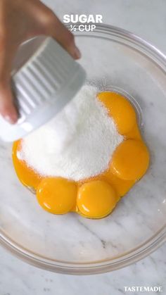 someone is adding sugar to eggs in a bowl