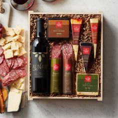 an assortment of meats, cheese and wine in a wooden box on a table