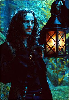 a man with long hair standing next to a lantern