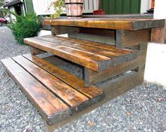 two wooden benches sitting next to each other on top of gravel covered ground with potted plants in the background