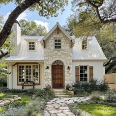 a white house with brown shutters and stone walkway leading to the front door is surrounded by greenery