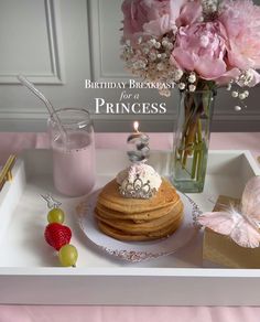 a birthday cake on a tray with pink flowers in a vase and other items around it