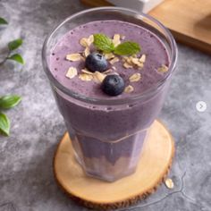 a smoothie with blueberries and granola on top is sitting on a wooden coaster