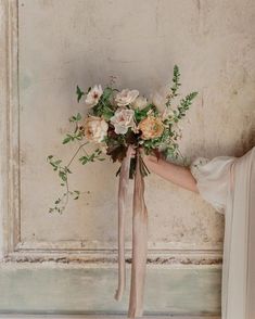 a woman holding a bouquet of flowers in front of an old wall with peeling paint