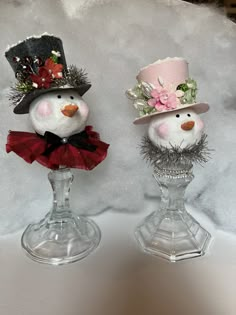 two snowmen wearing hats and sitting on top of each other in glass vases