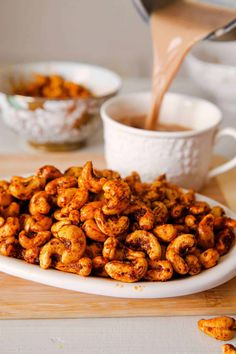 a white plate topped with fried nuts next to a cup of coffee and bowl of sauce